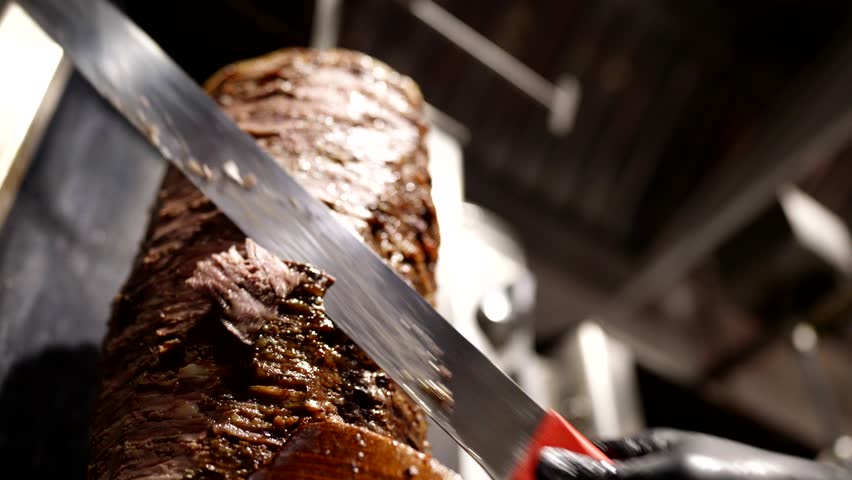 Close-up of sharp knife slicing juicy layers of grilled shawarma meat under warm light.