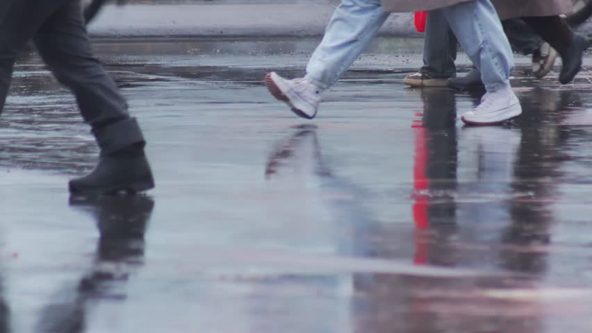 Feet of people in autumn shoes cross a wet road and puddles in autumn weather. Wet feet and shoes. Slow motion