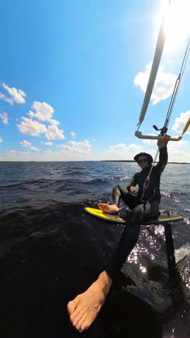 Kiteboarder Sitting On Hydrofoil Board While Gripping Control Bar Of Kite. vertical shot