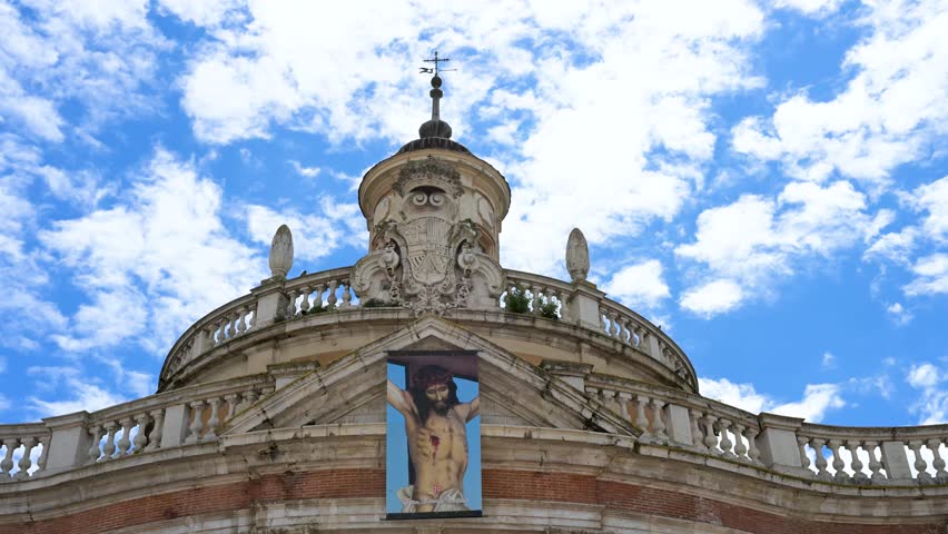 ARANJUEZ, SPAIN - Exterior detail of the top of the historic Royal Church of San Antonio de Padua, featuring a banner of Jesus Christ against a partly cloudy sky.