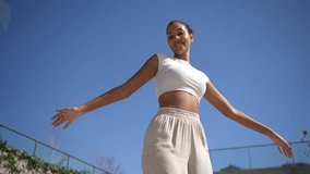 An empowered woman confidently walks outdoors under a clear blue sky, wearing a chic crop top and relaxed pants, blending fashion and fitness elegantly while enjoying the fresh air - Powered by Shutterstock - Get 15% off with code: PIKWIZARD15
