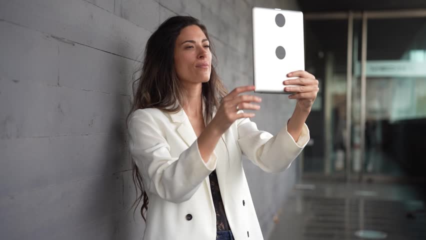 A confident, professional woman is taking a stylish selfie with her tablet in a sleek, contemporary office setting, showcasing the vibrant essence of modern work culture and collaboration