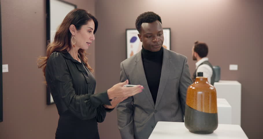 Woman, man and exhibition with tablet at art gallery for negotiation, explain and info for deal. People, presentation and customer with shopping, guide and display for price, sale and app at event