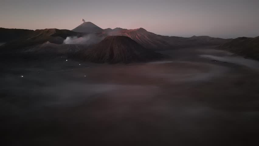 Epic aerial view at sunrise over Mount Bromo, located in East Java, Indonesia. This dramatic volcanic landscape features the iconic smoking crater of Mount Bromo, surrounded by a sea of sand and the d