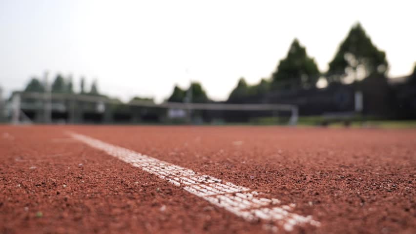 Tennis ball rolling across red clay court at local sports facility in afternoon sunlight