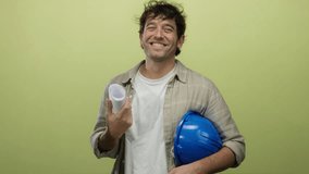 Hispanic man smiling holding blueprints and a hardhat against a green background, embodying the confident and professional demeanor of an architect or engineer. - Powered by Shutterstock - Get 15% off with code: PIKWIZARD15