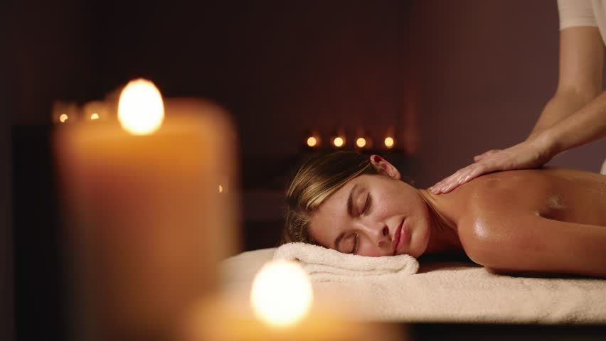 A Young and Beautiful Woman Gets a Relaxing Massage in a Spa. The Environment Is Surrounded by Candles that Create Atmosphere and Help to Relax. Concept of Women