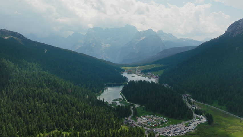 Scenic aerial of mountain lake Lago Di Misurina in Dolomites with green hills and cloudy summer sky, ascend