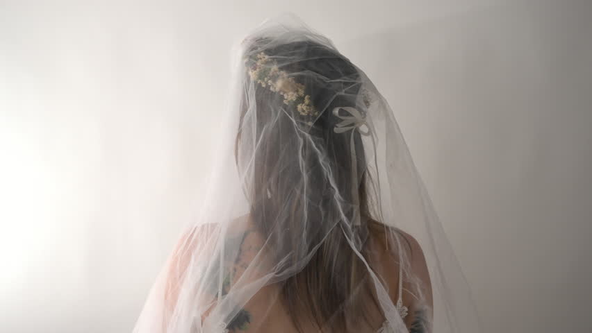 The camera tracks in on the bride as she slowly turns to face it. Her neutral gaze adds a sense of calm and poise, creating an intimate and serene moment.