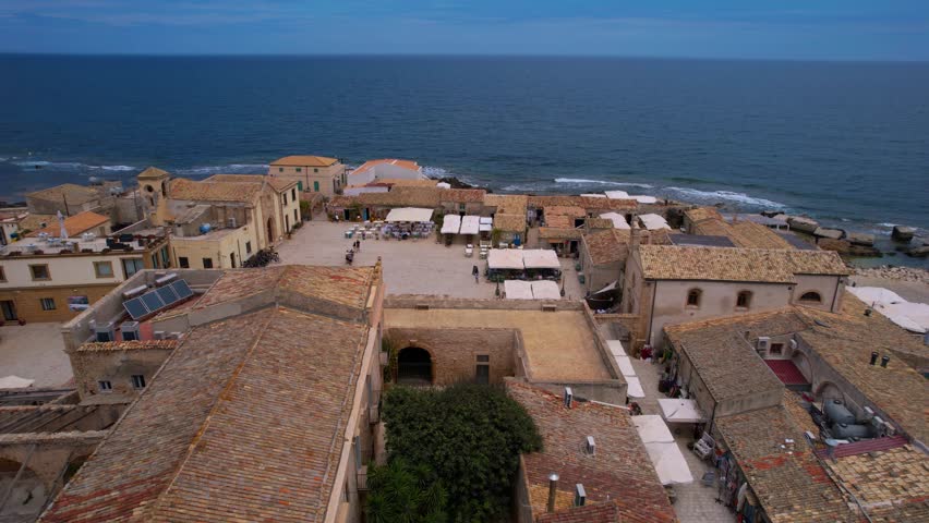 Scenic drone flyover of Marzamemi in Sicily, Italy. Fishing boats, tiled roofs, and seaside charm.