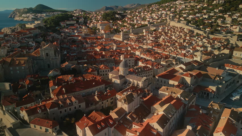 Medieval style buildings with red roofs in old city of Dubrovnik lit by sunlight camera moving around. Famous tourist location on Adriatic sea coast aerial panorama. Travel trends