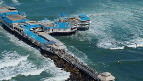 Pier extending into turquoise ocean along La Rosa Nautica Lima Peru from above in tropical weather with surfers catching waves - Powered by Shutterstock - Get 15% off with code: PIKWIZARD15