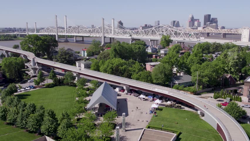Drone shot of the Louisville, Kentucky skyline featuring the walking bridge and Ohio River under bright, sunny skies. Perfect for tourism and cityscape content.