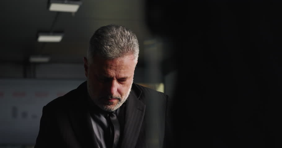 Frustrated businessman holding back emotion while running hand through hair in tense office meeting during corporate setback