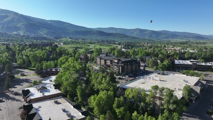 Steamboat Springs Colorado 2025 Spring drone shot with a hot air balloon over the village toward the base of the mountain. Condos and bright green spring colors.