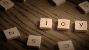 Wooden scrabble-style tiles spell joy as the camera pans smoothly across a rustic wooden surface with warm lighting. - Powered by Shutterstock - Get 15% off with code: PIKWIZARD15