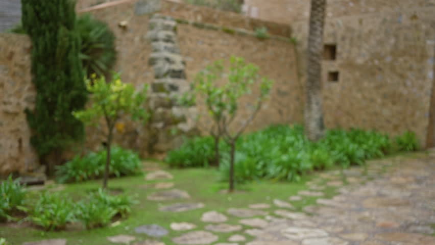 Blurred view of a charming mediterranean garden with stone path and ancient walls, exuding a serene atmosphere under soft, natural light.