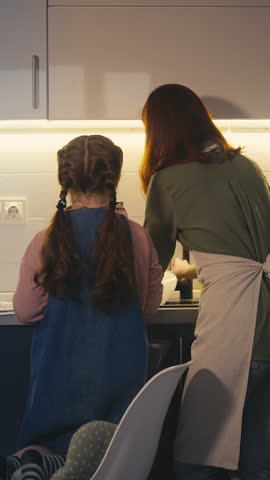 Little girl helping mom wash dishes in kitchen, learning household chores