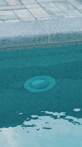 Clear blue water in the swimming pool. Close-up of a recessed underwater light. The edge of the pool is finished with gray curbstone. Relaxation in the backyard of a country house
