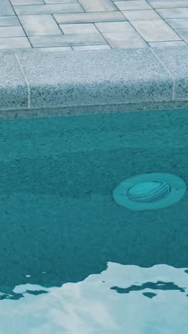 Clear blue water in the swimming pool. Close-up of a recessed underwater light. The edge of the pool is finished with gray curbstone. Relaxation in the backyard of a country house
