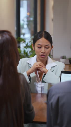 Young Asian businesswoman presenting a sales report to colleagues during a team meeting in a modern office. Confident female leader engaging in professional communication, explaining data and strategy