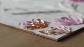 Applying Gold Leaf to Textured Floral Artwork - Fingers delicately place gold foil onto textured pink petals of a handmade floral painting. - Powered by Shutterstock - Get 15% off with code: PIKWIZARD15