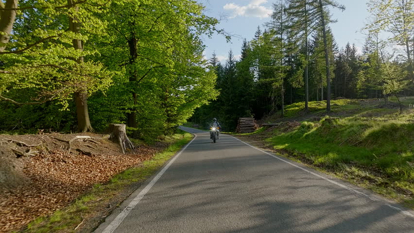 Driver riding motorcycle on empty asphalt road, spring mountains during sunset