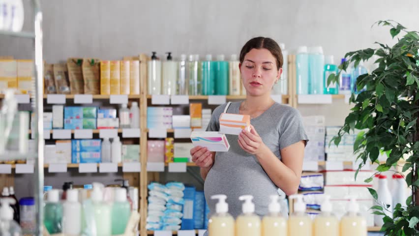 Focused pregnant woman choosing pill box and making decisions about pharmaceuticals and health care in small pharmacy
