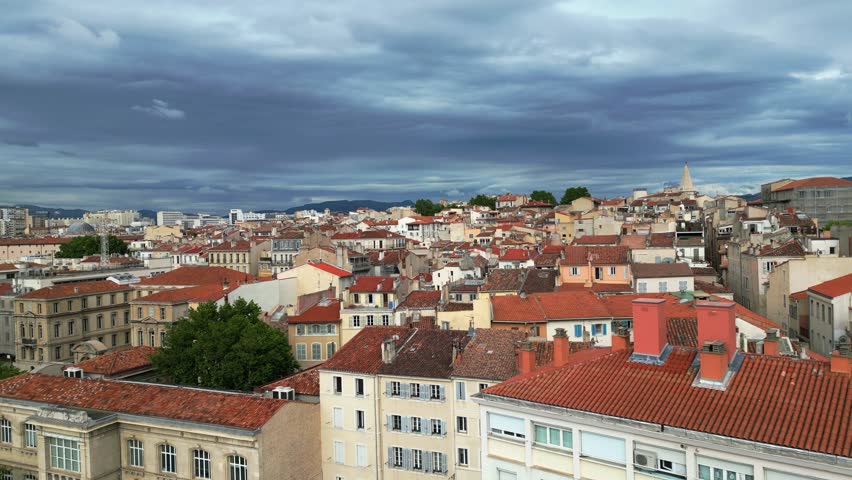 Aerial view of Marseille, France, showcasing the port, rooftops of buildings, and the distant Cathédrale La Major under a cloudy sky. Corporate presentations, news reports, city branding reels