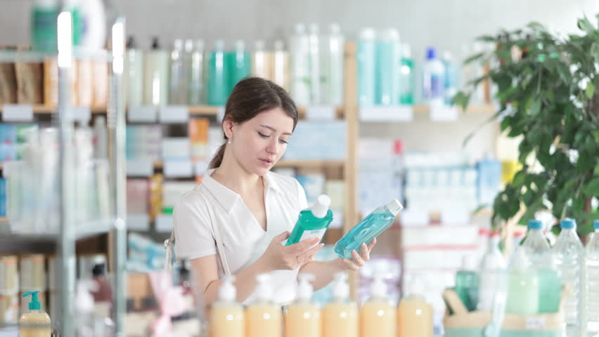 Young woman choosing mint mouthwash at pharmacy. European woman chooses products for the care of teeth. High quality 4k footage