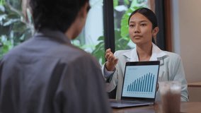 Confident Asian businesswoman presenting a marketing plan using a laptop during a business meeting in a casual café setting. Team collaboration, project strategy, and modern workplace concept. - Powered by Shutterstock - Get 15% off with code: PIKWIZARD15