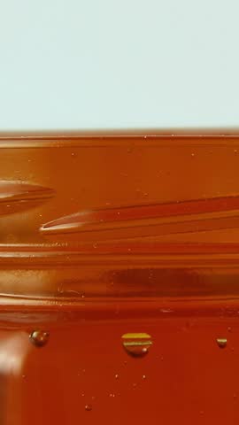 A wooden honey spoon slowly rotates in a circular motion in thick golden honey. Creating a smooth, thick stream of sweet food. Asmr. macro photography.
