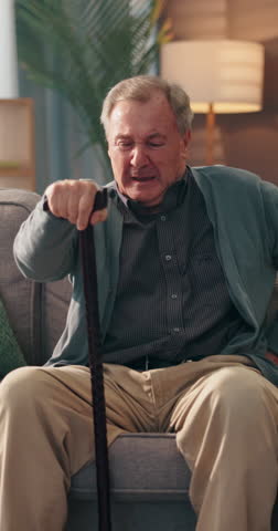 Senior man, cane or back pain on sofa with injury, scoliosis or osteoporosis with recovery in home. Elderly person with disability, walking stick or spine ache with mobility aid for balance in lounge