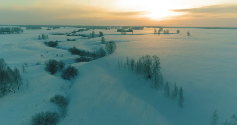 Drone aerial view of cold winter landscape arctic field, trees covered with frost snow, ice river and sun rays over horizon. Extreme low temperature weather. Siberia