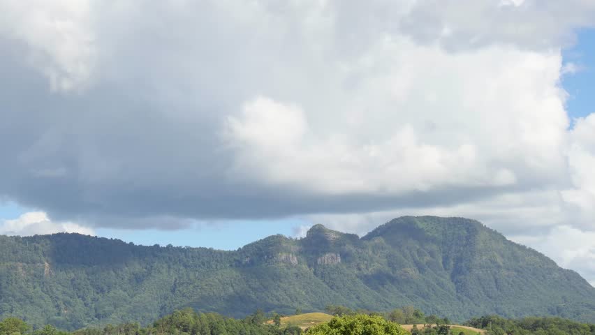 A serene view of lush green hills beneath a sky filled with fluffy white clouds.