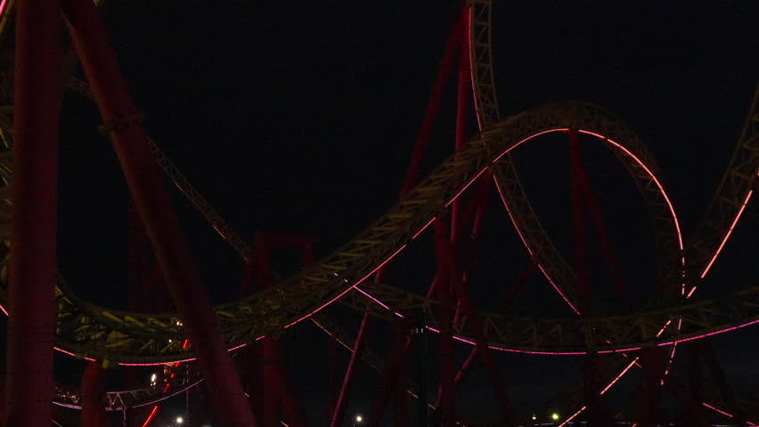 Rollercoaster Night Ride Amusement Park: Thrilling nighttime rollercoaster ride at an amusement park, showcasing dynamic curves and red lighting effects.