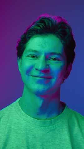 Happy Portrait of Young Man Looking at Camera and Smiling in Neon UV Colors of Filter. Shining Effect of Vivid Lighting and Backlight Illumination Inside Amazing Studio. Trendy Person with Cute Grin