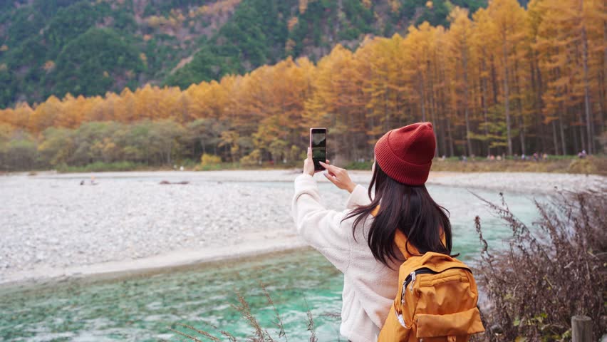 Young female tourist enjoying and taking a photo with beautiful autumn at kamikochi in Japan