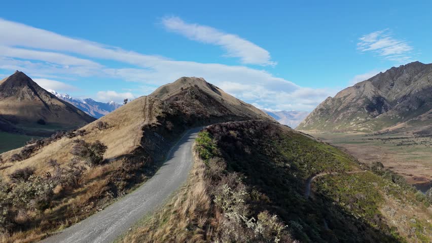 Aerial footage captures winding mountain roads and stunning landscapes in Queenstown, New Zealand, under clear blue skies