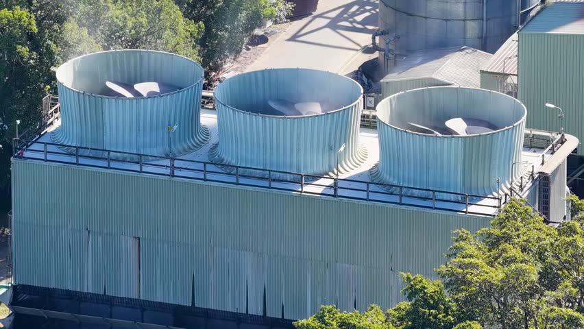 Aerial view of large industrial cooling fans on a factory rooftop surrounded by trees.