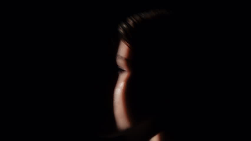 A striking side profile portrait of a person with half their face illuminated by soft light beam and deep shadows.