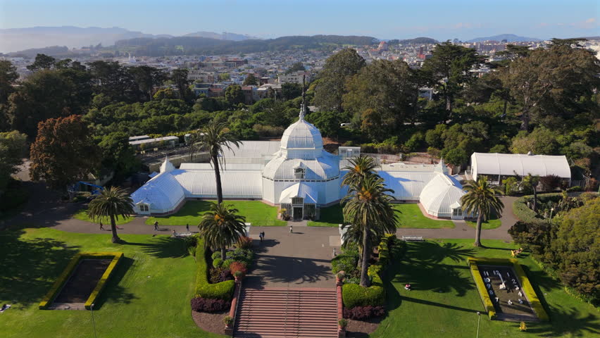 An aerial view shows a stunning white dome surrounded by lush San Franciscos Botanical Garden with blooming flowers, tall palm trees, rolling hills, creating serene landscape that invites tranquility