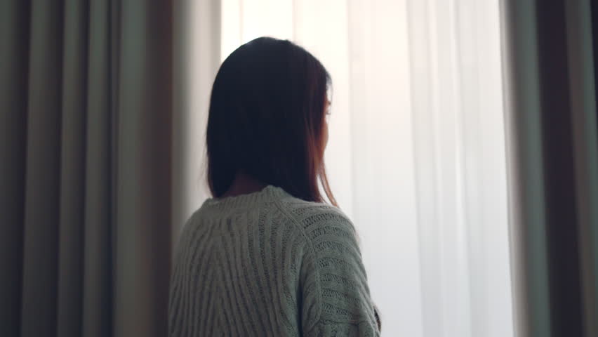 Happy young asian woman smiling and opening curtains to let morning sunlight into the room – fresh new day, hope, positive mindset and peaceful lifestyle at home with natural light and bright energy