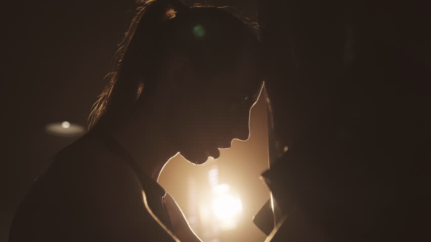 Exhausted female fighter leaning on punch bag in gym, silhouette in dark ring. Tired athletic woman breathing hard after intense cardio workout, female beauty and power, self-defense classes for women