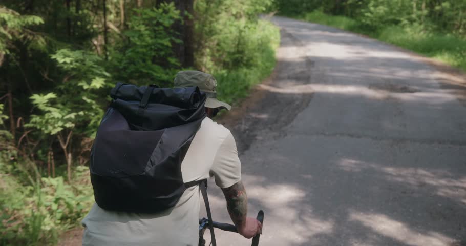 Over-the-shoulder shot of a solo male cyclist riding through a winding forest road. His backpack and hat suggest long travel, highlighting independence and immersive nature experience. High quality 4k