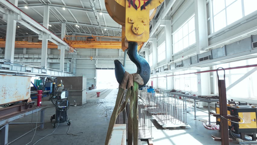 Hook of traveling gantry crane inside of industrial metalwork workshop. Handheld real time footage