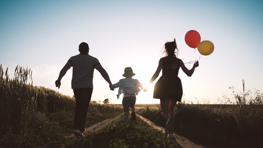 Joyful little boy holding hands of parents and running on field, rear view. Happy childhood moments, slow motion with people enjoying simple life, carefree child with mother and father in summer
