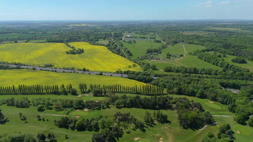 Aerial drone shot of yellow rapeseed fields and motorway with traffic passing through green landscape near Stevenage England UK Spring time