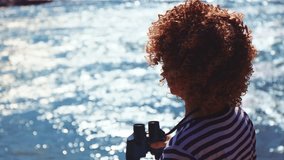 A person with curly hair stands by the water's edge, looking through binoculars as sunlight glimmers on the lake's surface. The peaceful setting invites exploration and curiosity. - Powered by Shutterstock - Get 15% off with code: PIKWIZARD15