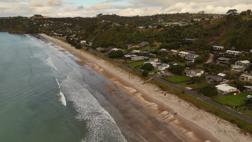 Aerial establishing shot of New Zealand, Waiheke Island, Onetangi Beach at golden sunrise. Villas and mansion in beachfront with green trees.